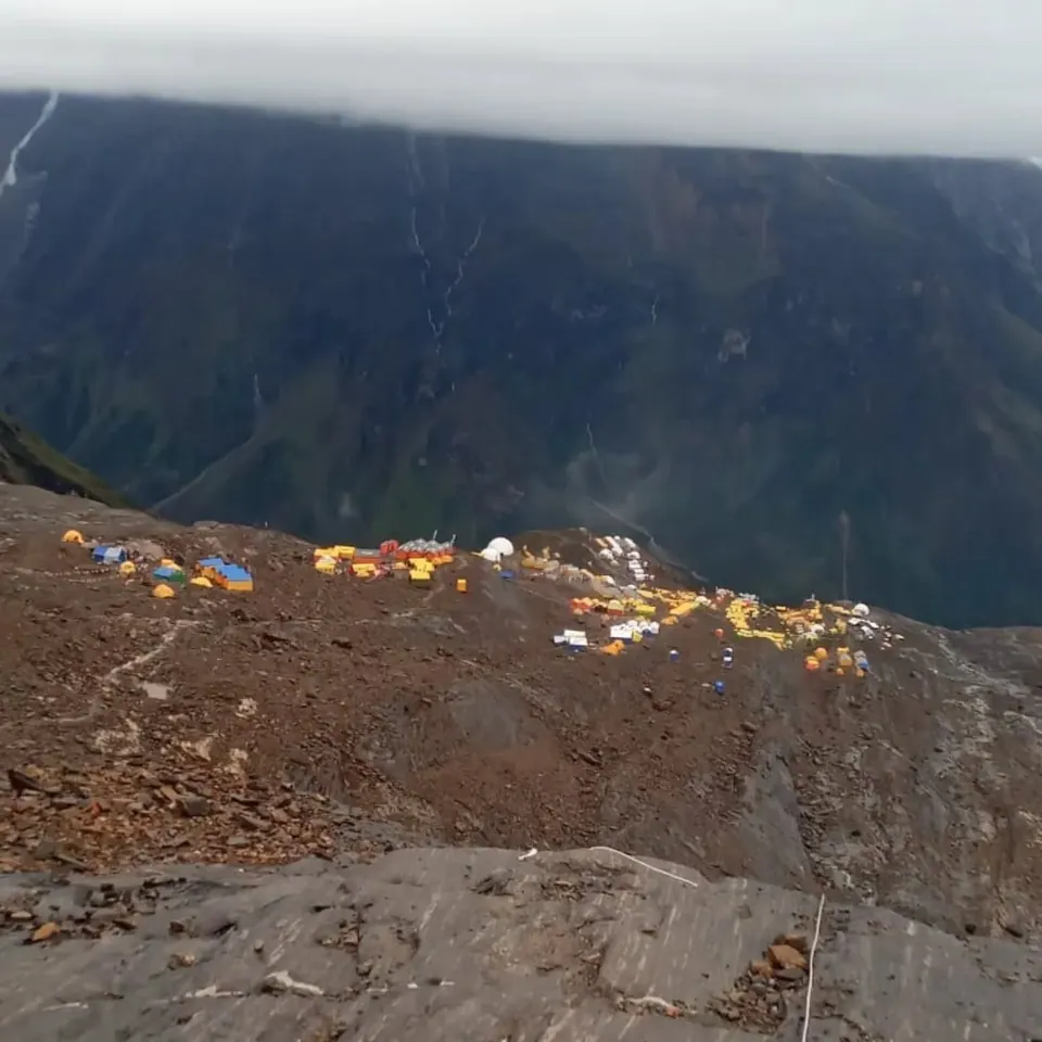 Expedition tents on a rocky glacier slope above a deep valley under low cloud, Manaslu Base Camp